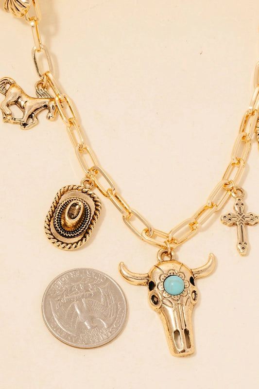 Gold charm necklace with various charms including a bull head and cross on a beige background.