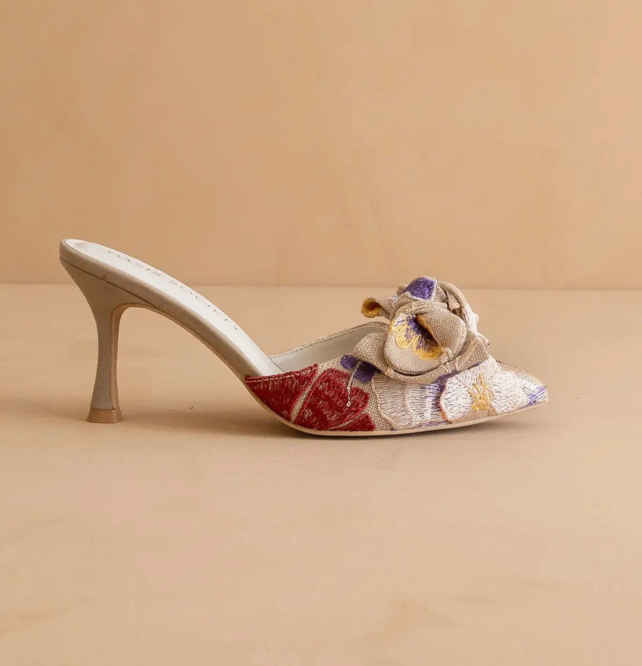Up close image of one tapestry floral design slip on a high heel shoe on a beige background