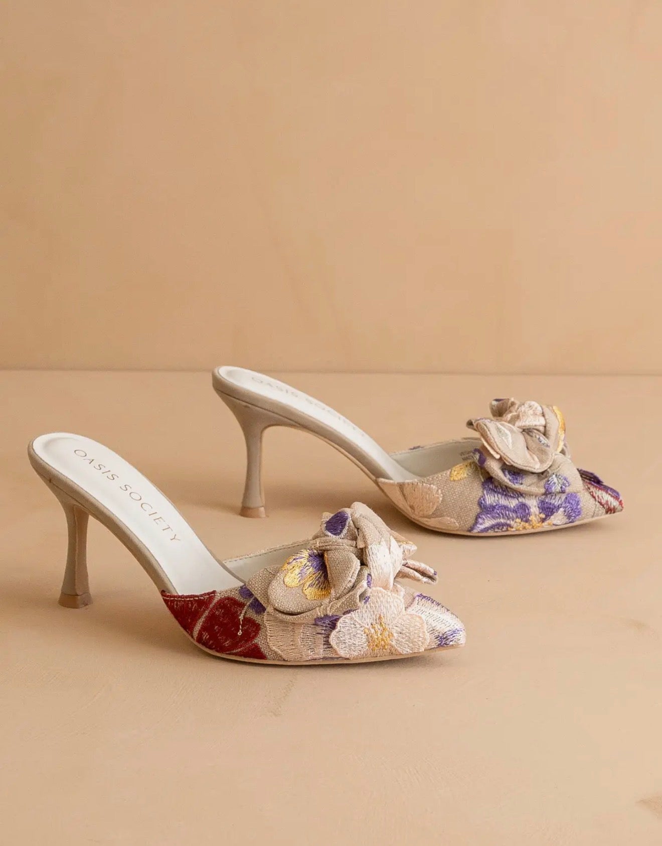 Pair of floral tapestry high-heeled  slip on shoes on a beige background