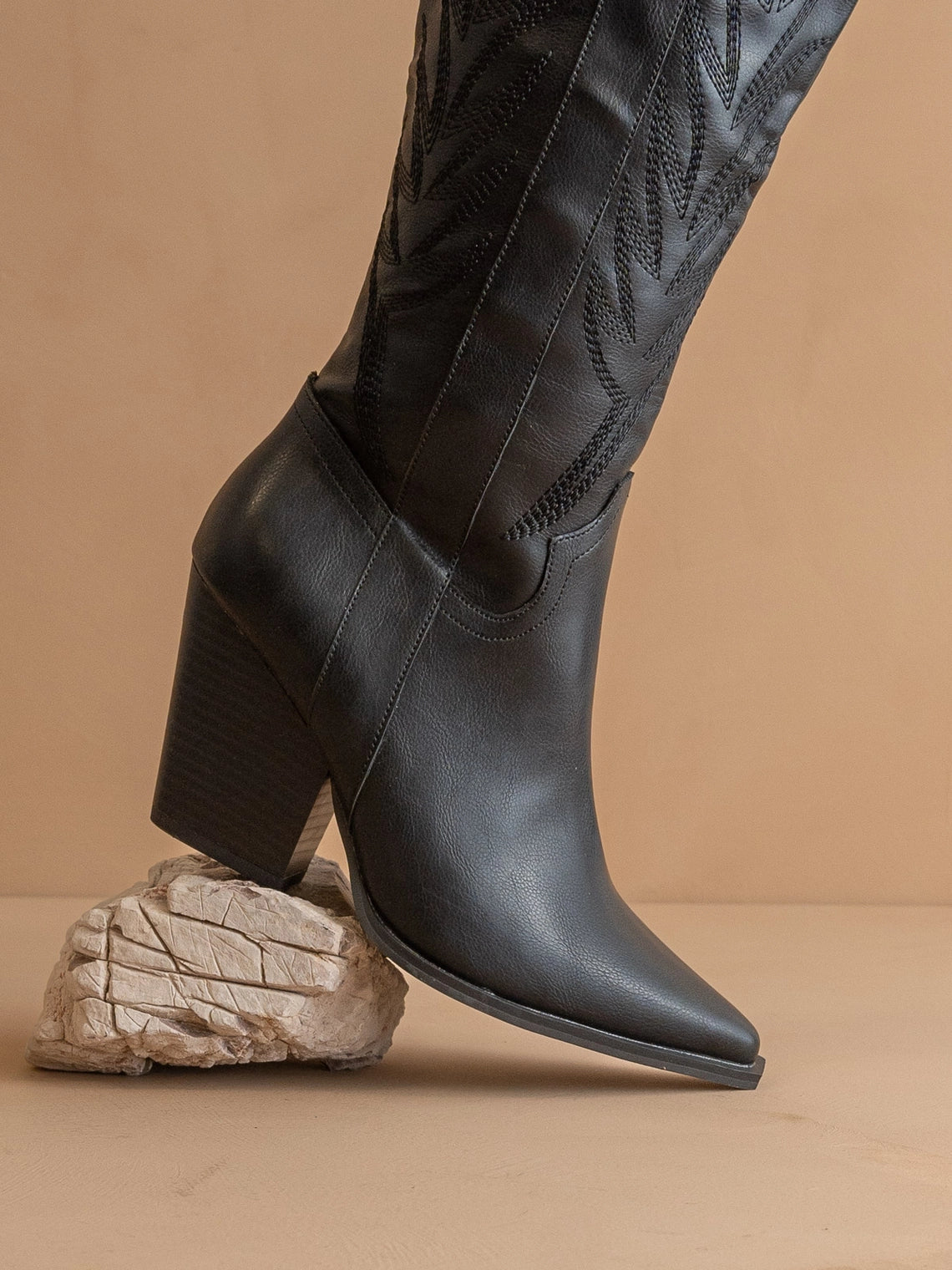 Black leather western boots with a textured pattern on a beige background