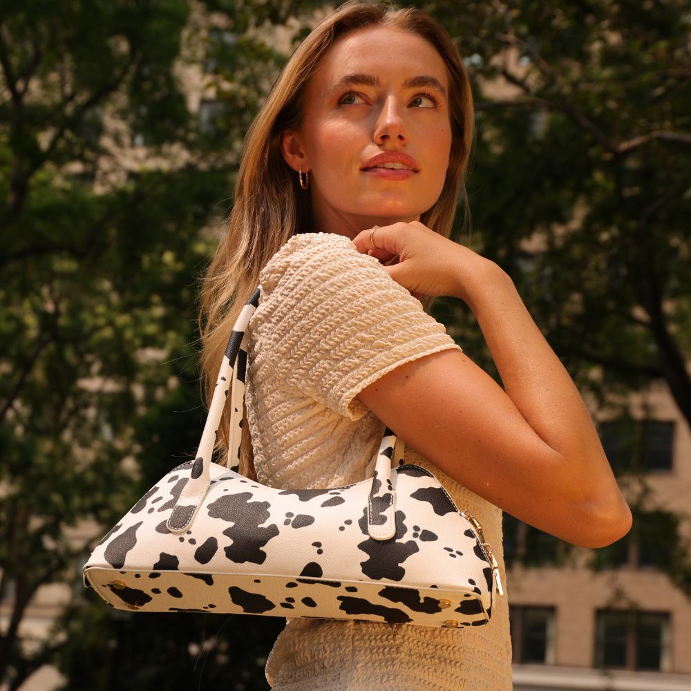 Woman holding a cow print handbag outdoors with trees in the background