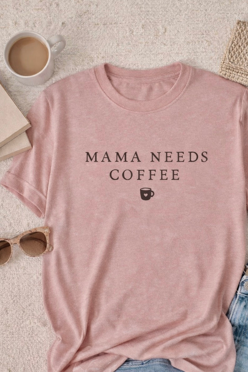 Muted Pink t-shirt with 'MAMA NEEDS COFFEE' text on a light surface with a cup of coffee, sunglasses, and book.