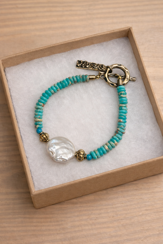 African Turquoise (Jasper) beaded bracelet with large coin pearl and a gold clasp in a jewelry box on a wooden surface