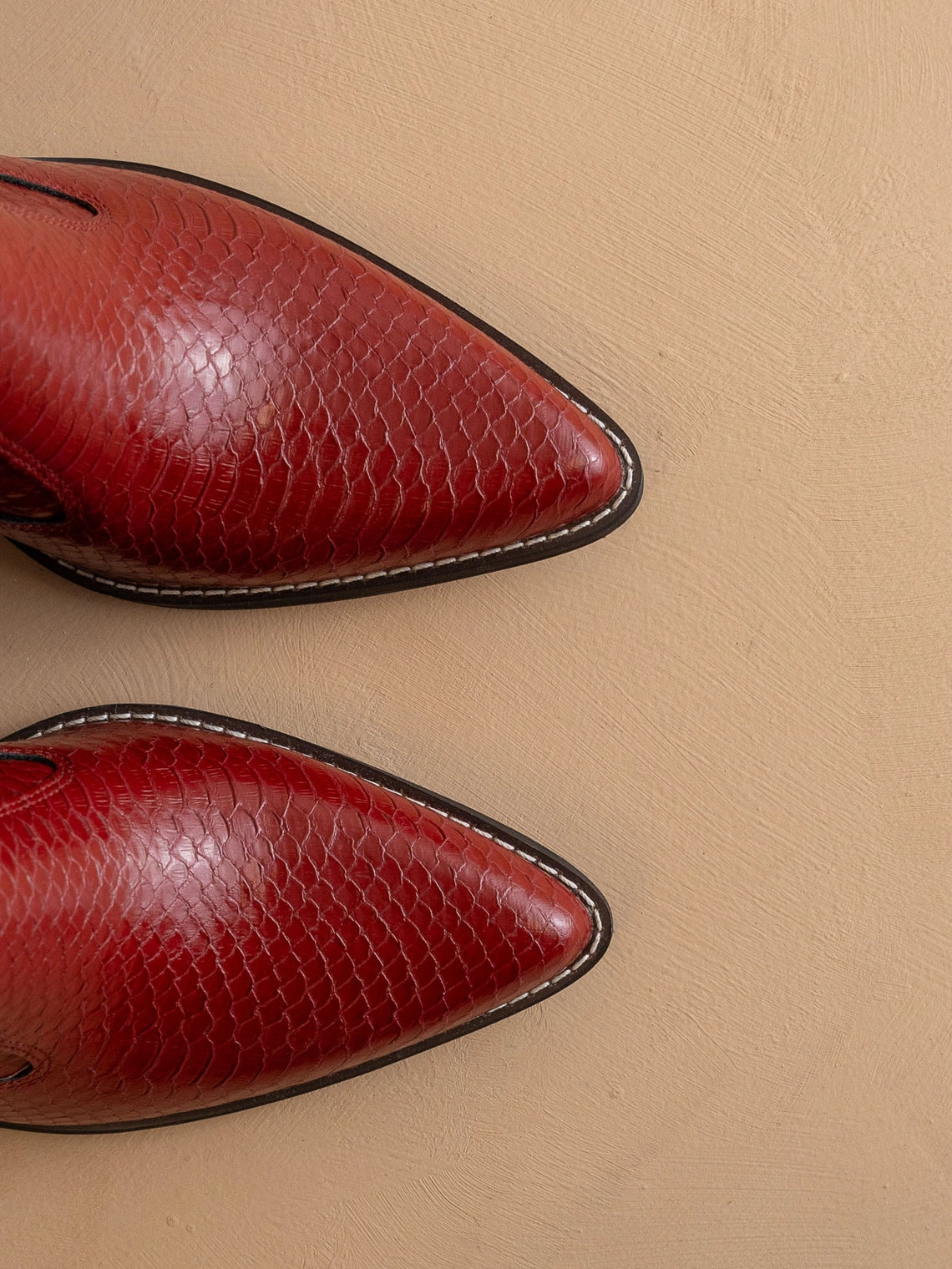 Pair of red pointed-toe snake skin embossed tip of boots on a beige background
