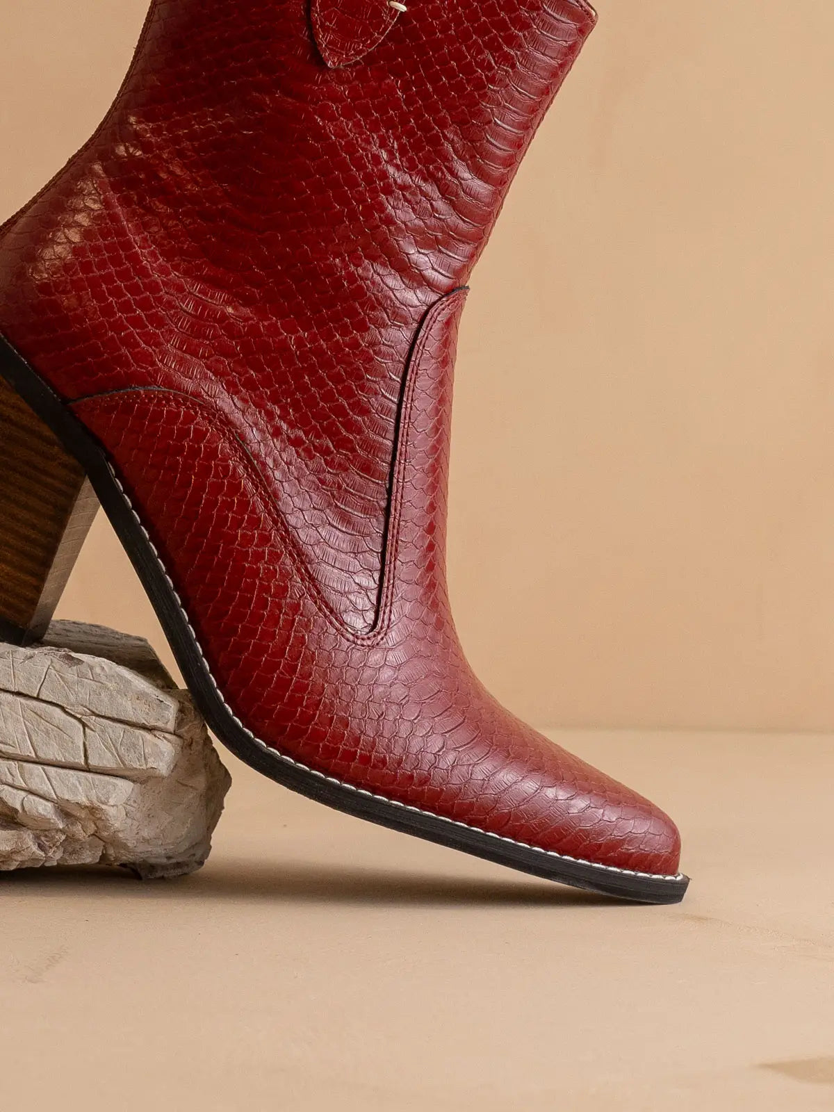 Red leather boot with a snake skin textured pattern on a beige background